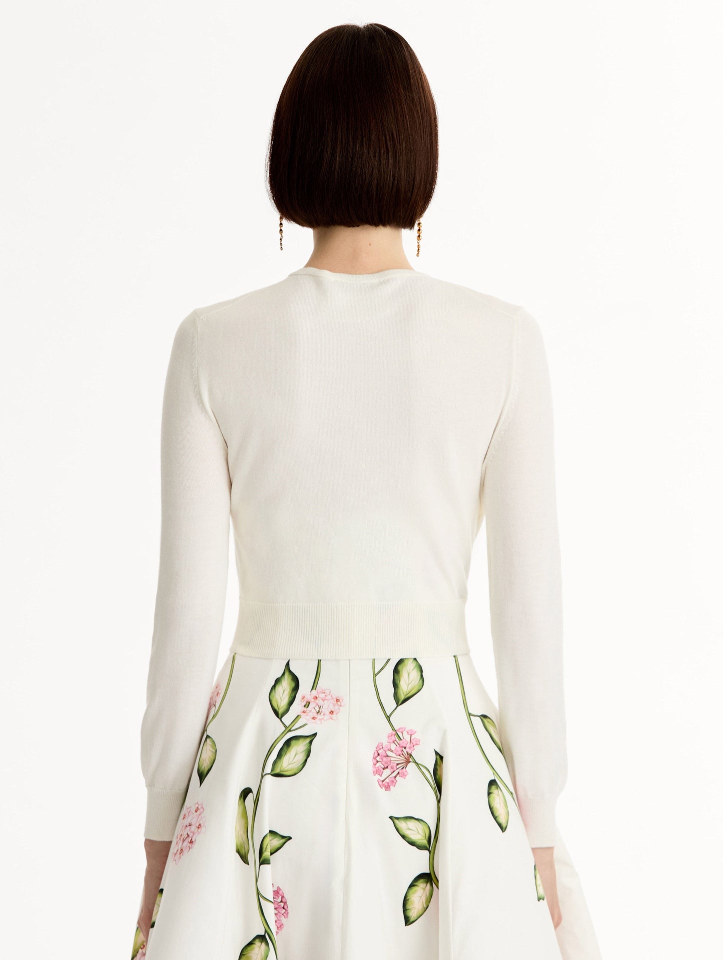 Ivory cropped cardigan with pink flower detailing stitched along the neckline and shoulder. Classic button closure. Crew Neck. Back View.