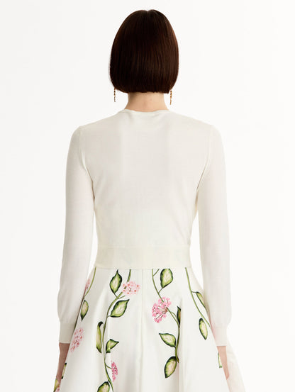 Ivory cropped cardigan with pink flower detailing stitched along the neckline and shoulder. Classic button closure. Crew Neck. Back View.