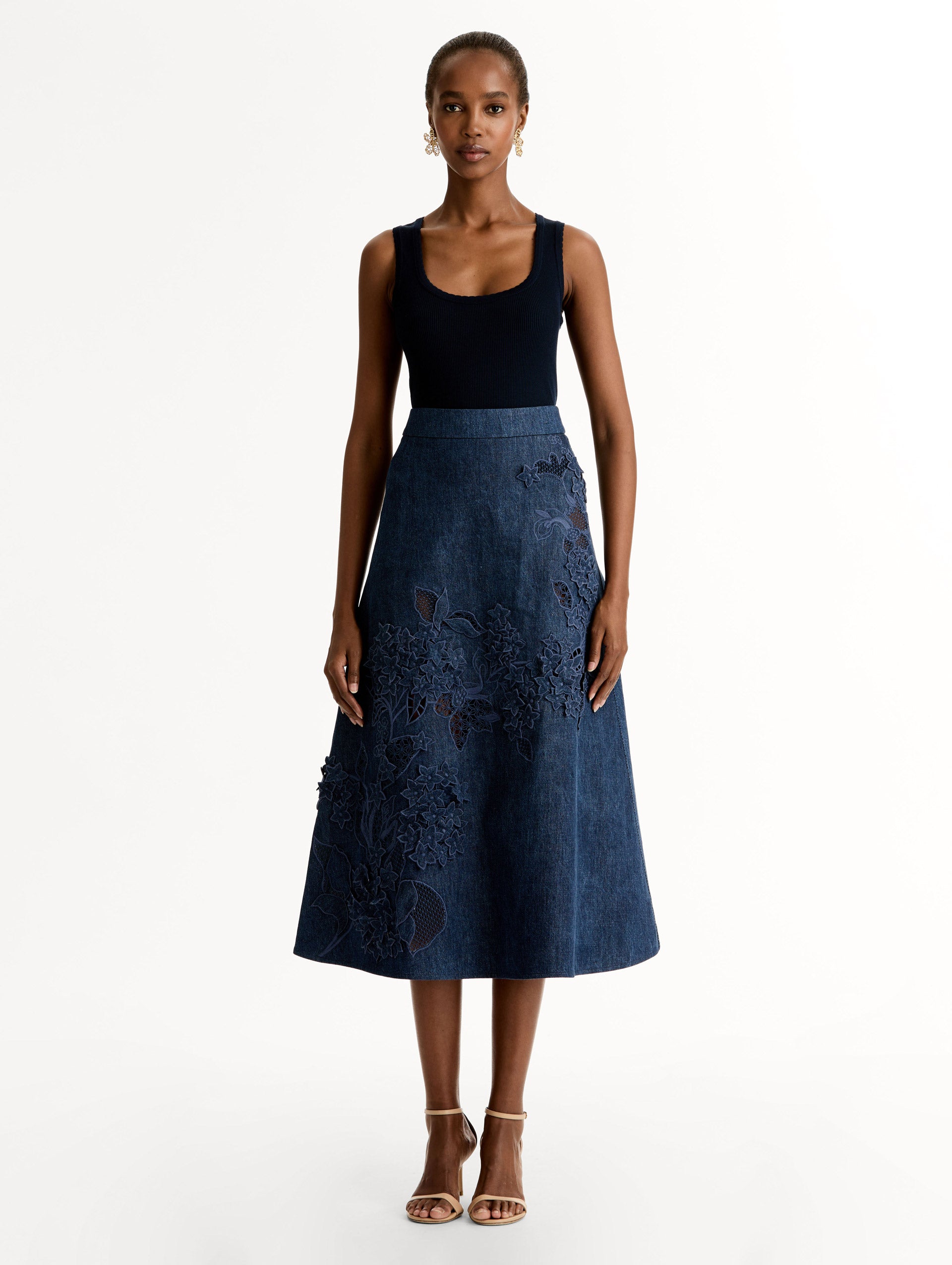 High waisted denim skirt with intricate porcelain flower threadwork. Classic A-line silhouette. Mid length. Front View.