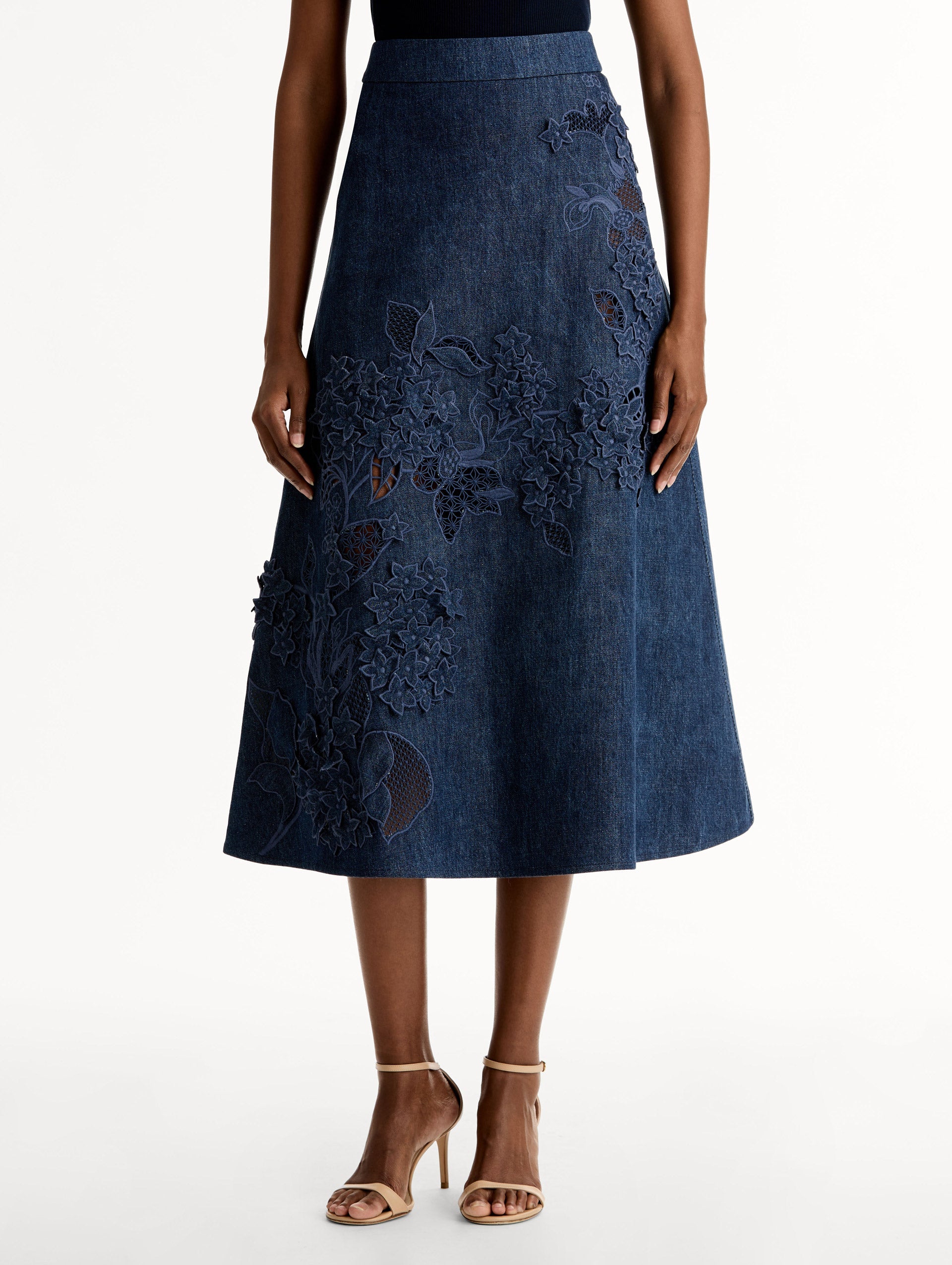 High waisted denim skirt with intricate porcelain flower threadwork. Classic A-line silhouette. Mid length. Front View.