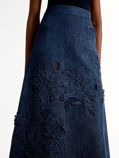 High waisted denim skirt with intricate porcelain flower threadwork. Classic A-line silhouette. Mid length. Side View, Close Up.