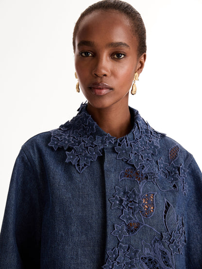 Cropped denim jacket with intricate porcelain flower threadwork and cutout detailing across the front and collar. Long sleeve. Front View, Close Up.