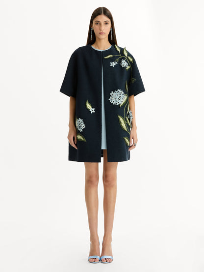 Short sleeve, navy tweed coat with porcelain flower embroidery. Floral motifs cascade across the front. Front View.