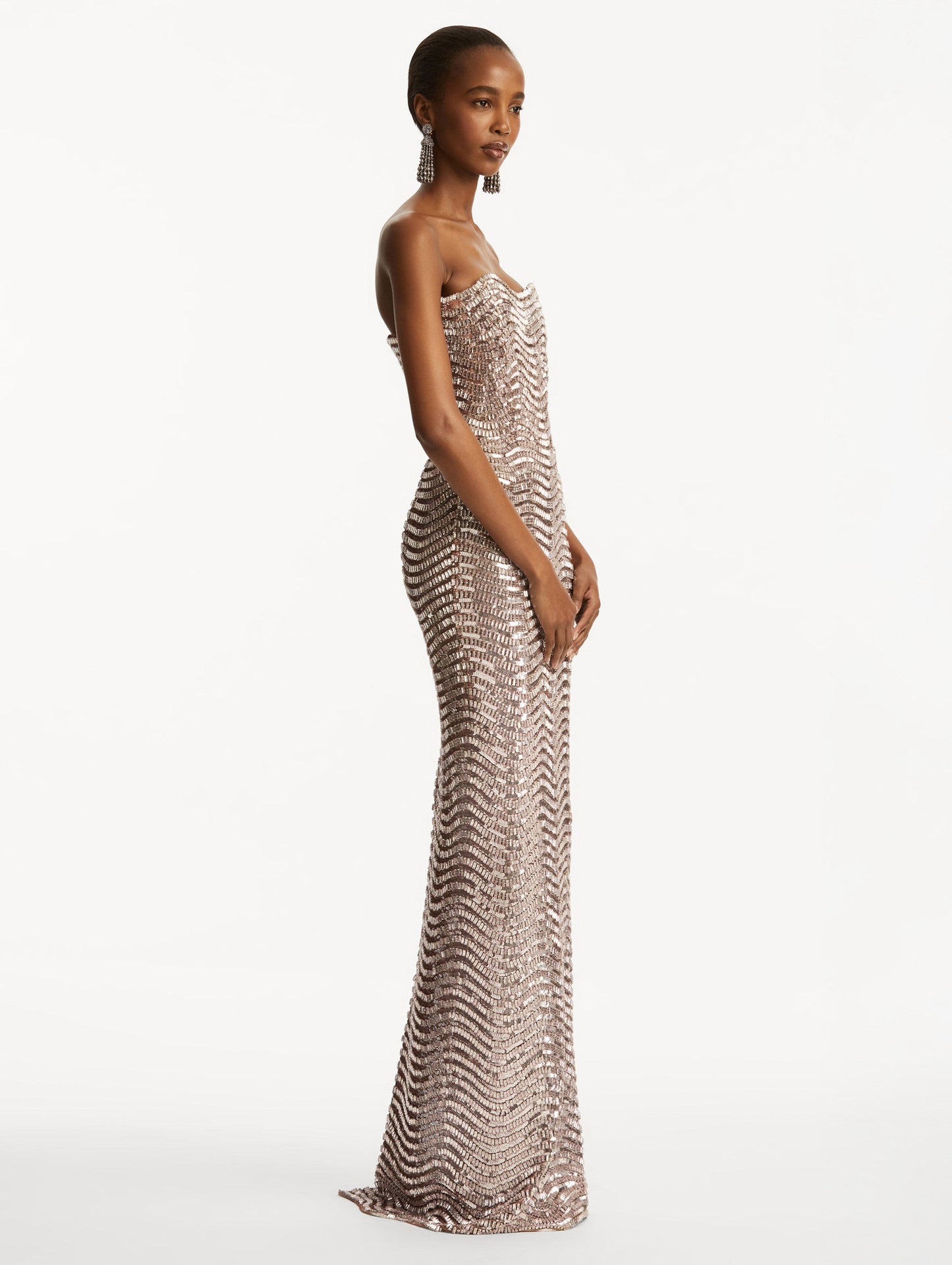 Model wearing soft pink strapless sequin wave embellished gown. Side view
