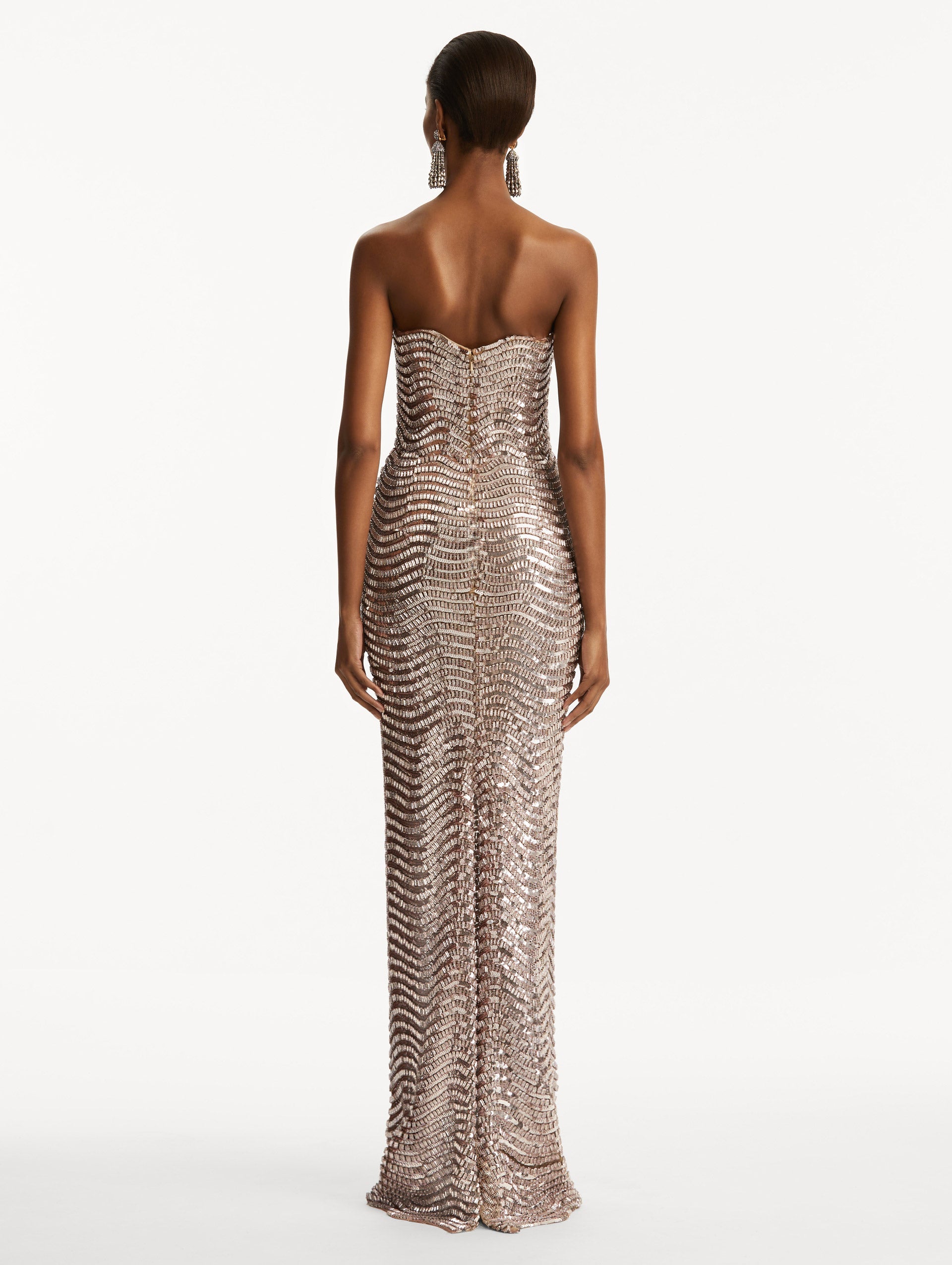 Model wearing soft pink strapless sequin wave embellished gown. Back view