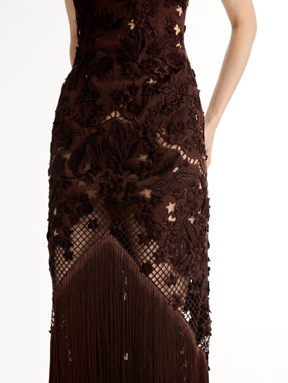 Mahogany strapless floor length gown with Porcelain flower threadwork in sculptural cutouts with glimpses of skin. Intricate lattice motifs. The silhouette elongates before cascading into a curtain of fringe. Front View, Close Up.