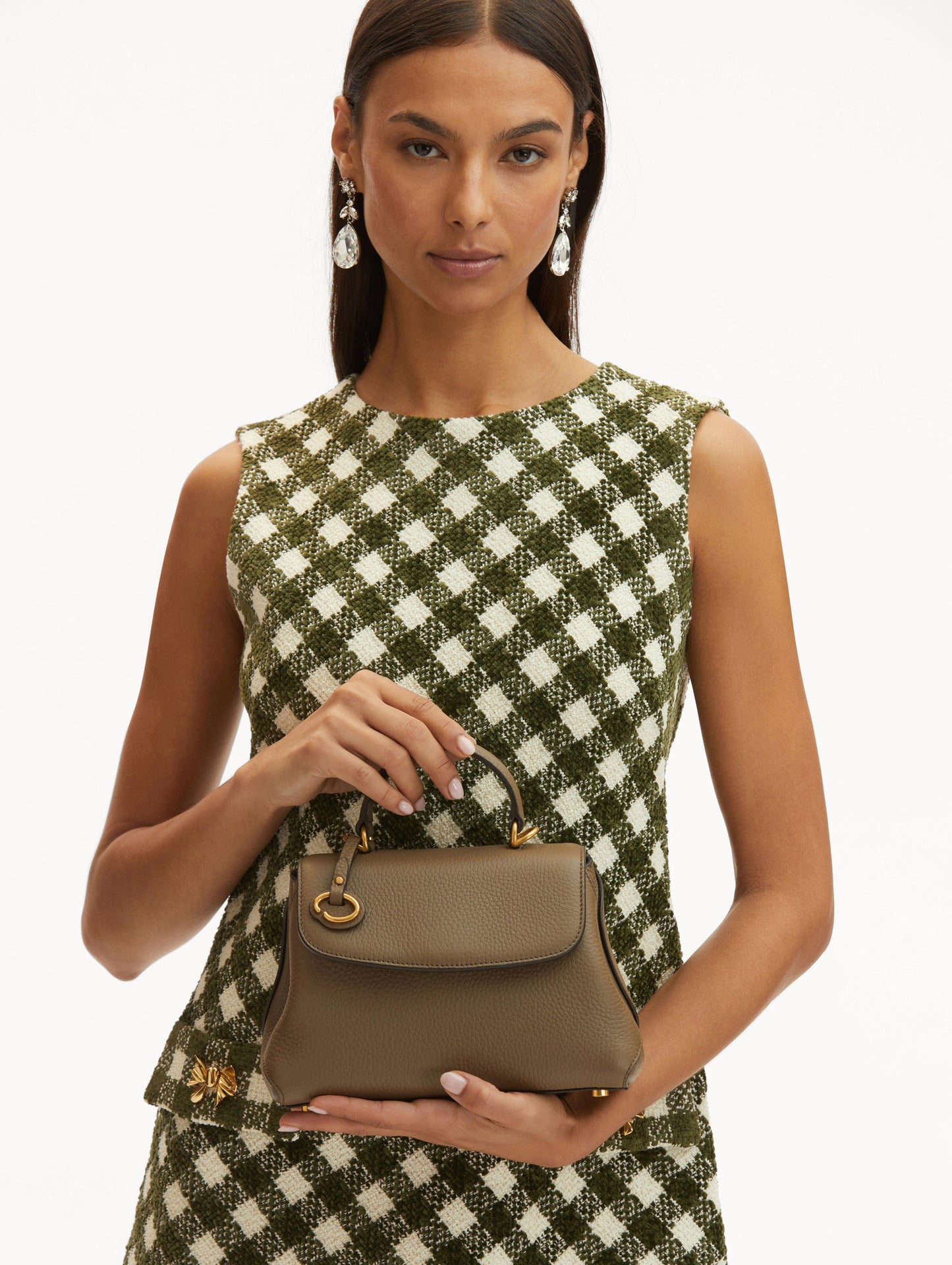 Model in plaid dress holding The Mini Poppy in taupe with O logo around the top handle. Front View