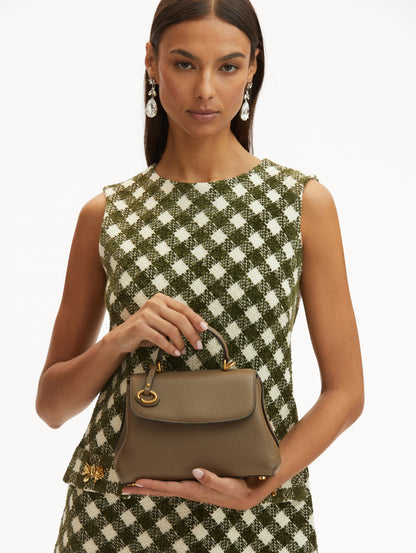 Model in plaid dress holding The Mini Poppy in taupe with O logo around the top handle. Front View