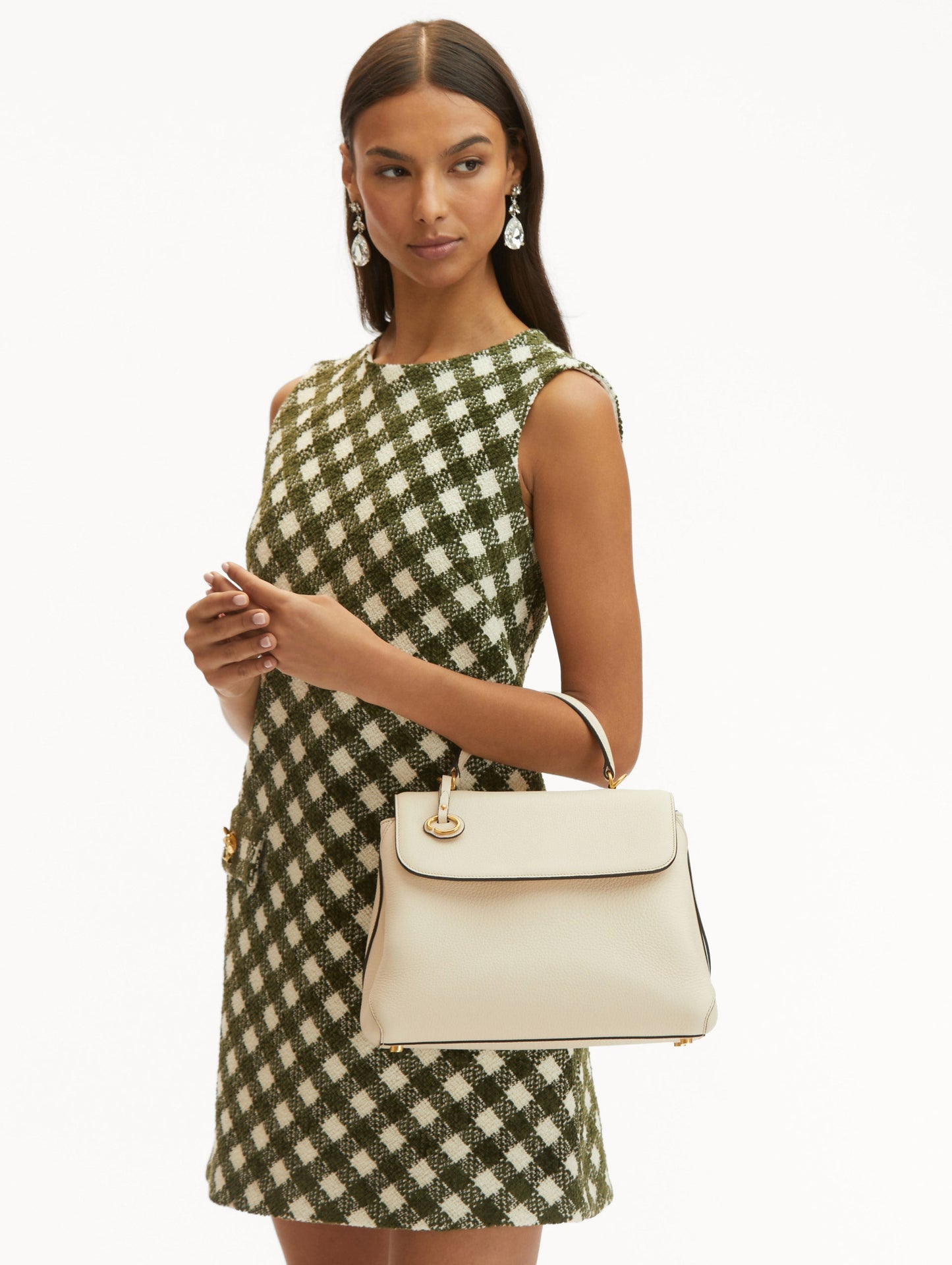 Model with plaid green and white dress holding The Poppy bag in white with top handle and O logo tag around the handle Front View