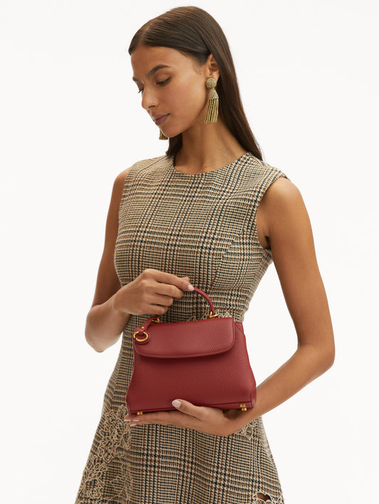 Model in plaid dress wearing The Mini Poppy in red with O logo around the top handle. Front View