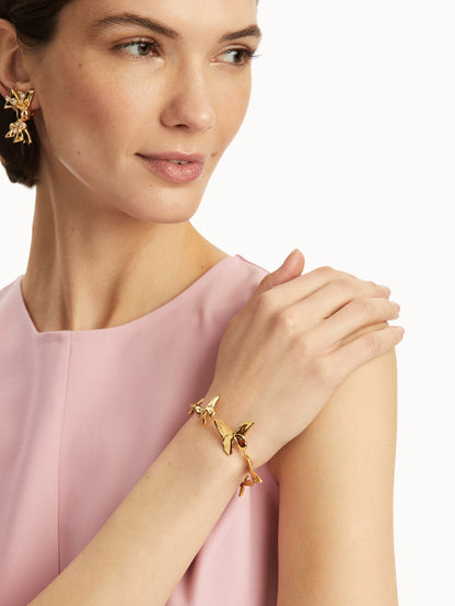 The model is wearing a gold butterfly necklace paired with a pink dress. Front view.