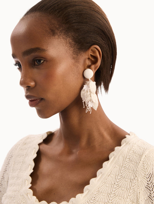 The model is wearing the Raffia Tassel Bouquet Clip-On Earrings in White. Detail View.