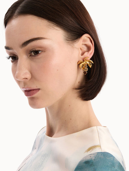 The model is wearing the Palm Leaf Clip-On Earrings in Gold with Crystal Trunks. Detail View.