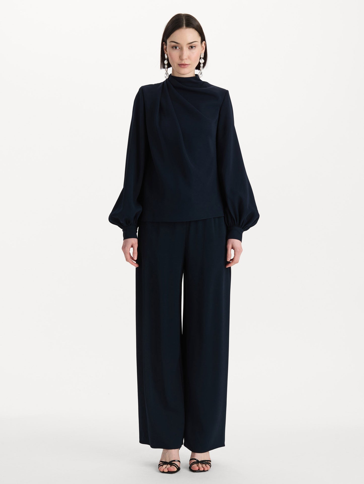 The model is wearing the Draped Georgette Blouse in the color Navy. Featuring silk georgette, a draping mock-neckline, and long, billowed sleeves. Front View.