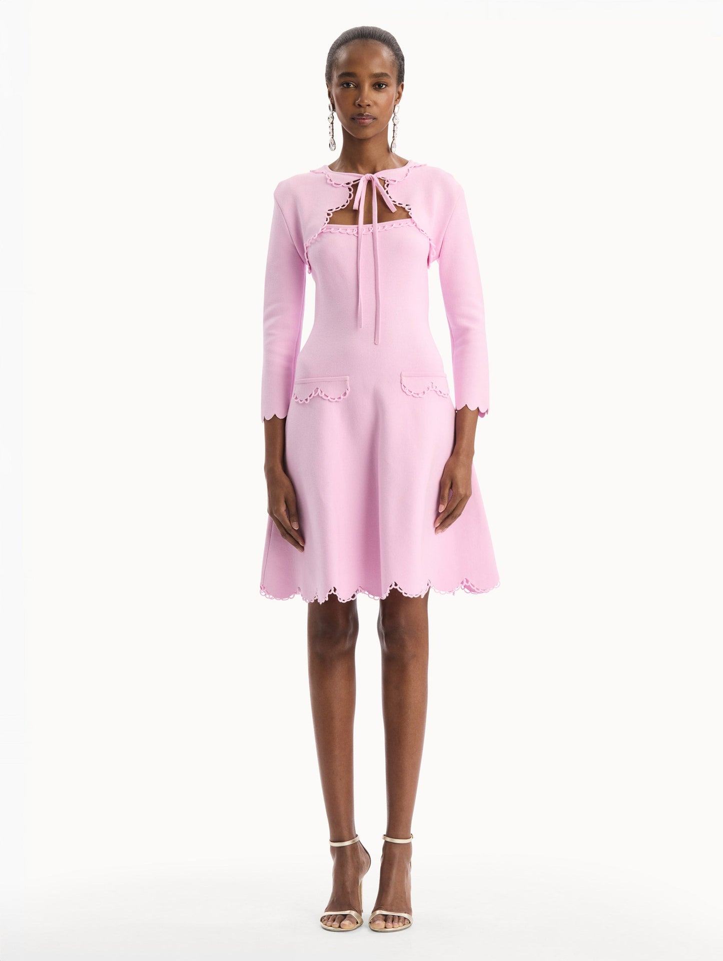 The model is wearing the Scallop Trim Knit Bolero with tie at front in the color pink. Front View.