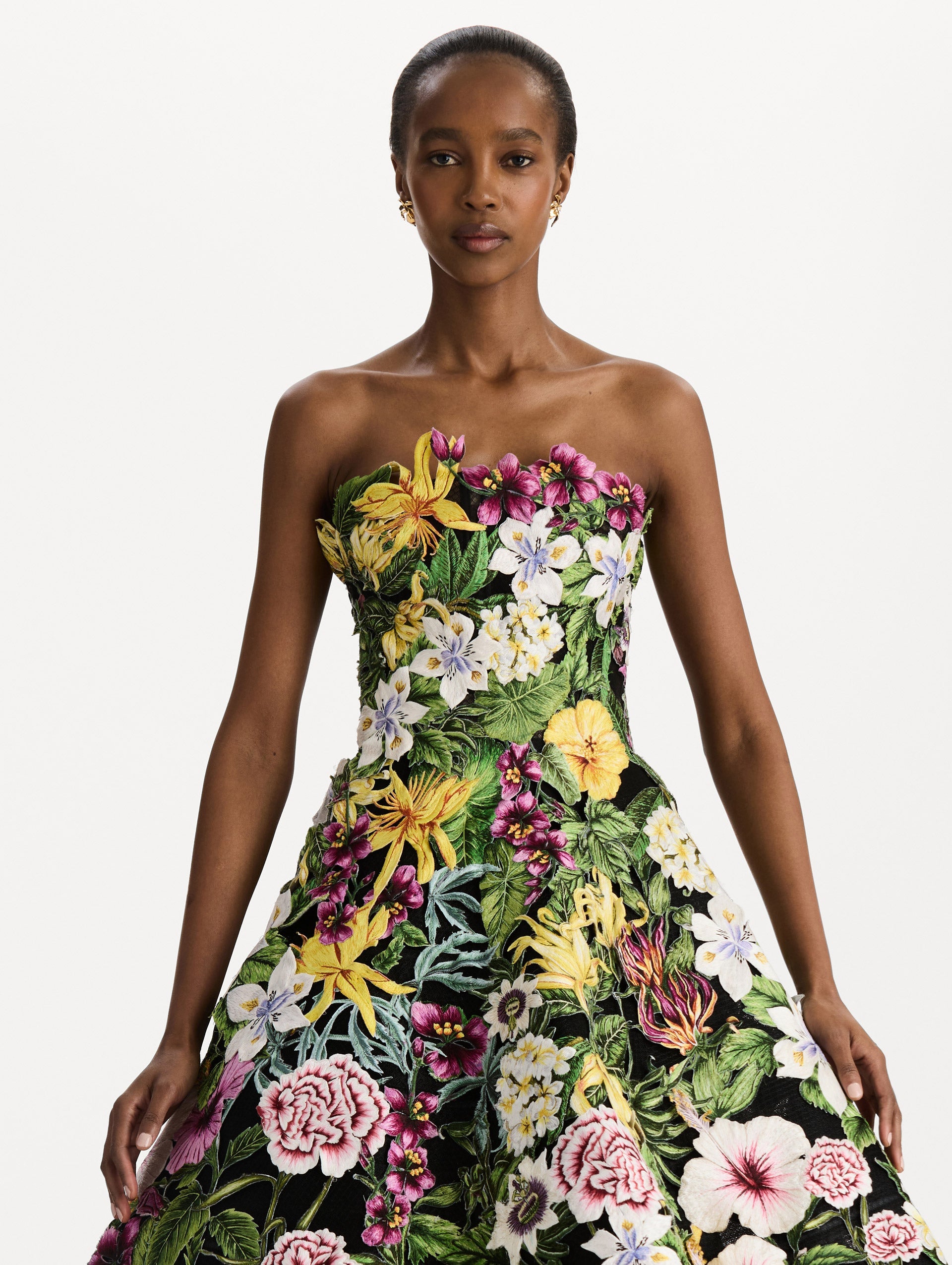The model is wearing the Dominican Mixed-Floral Guipure Gown. Featuring a strapless neckline, fitted bodice, and full skirt. Detail View.