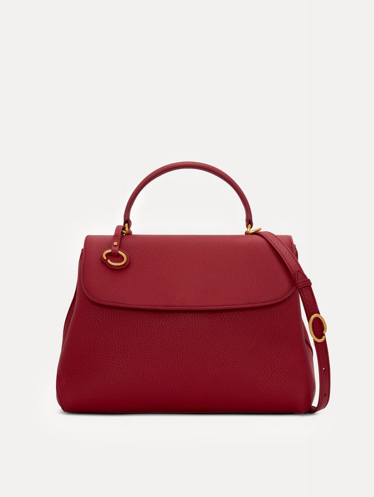 Model in plaid dress wearing The Poppy leather handbag in red with O logo around the top handle. Front View